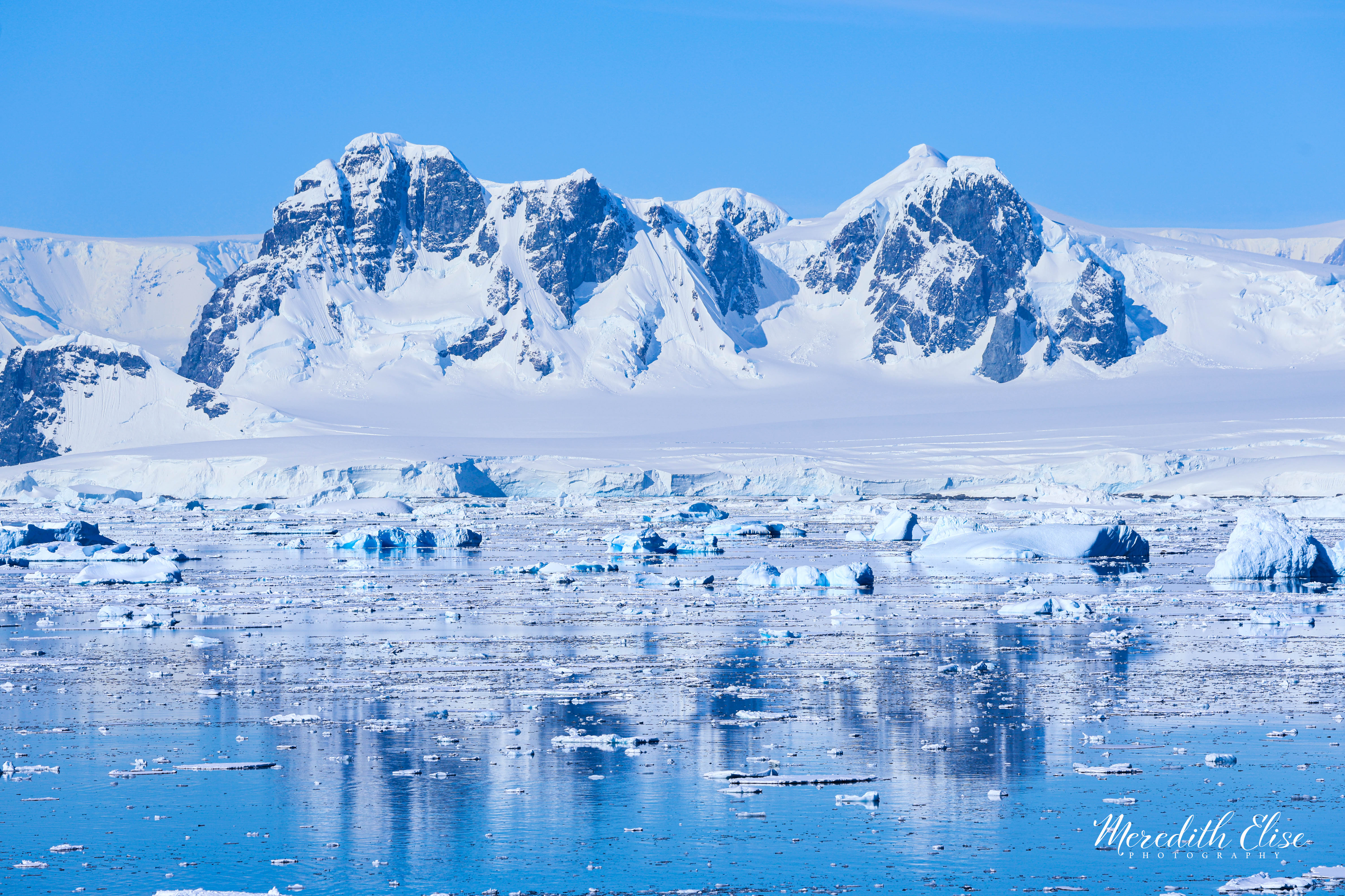 Jagged Antarctic peaks reflected in ice-flecked turquoise water