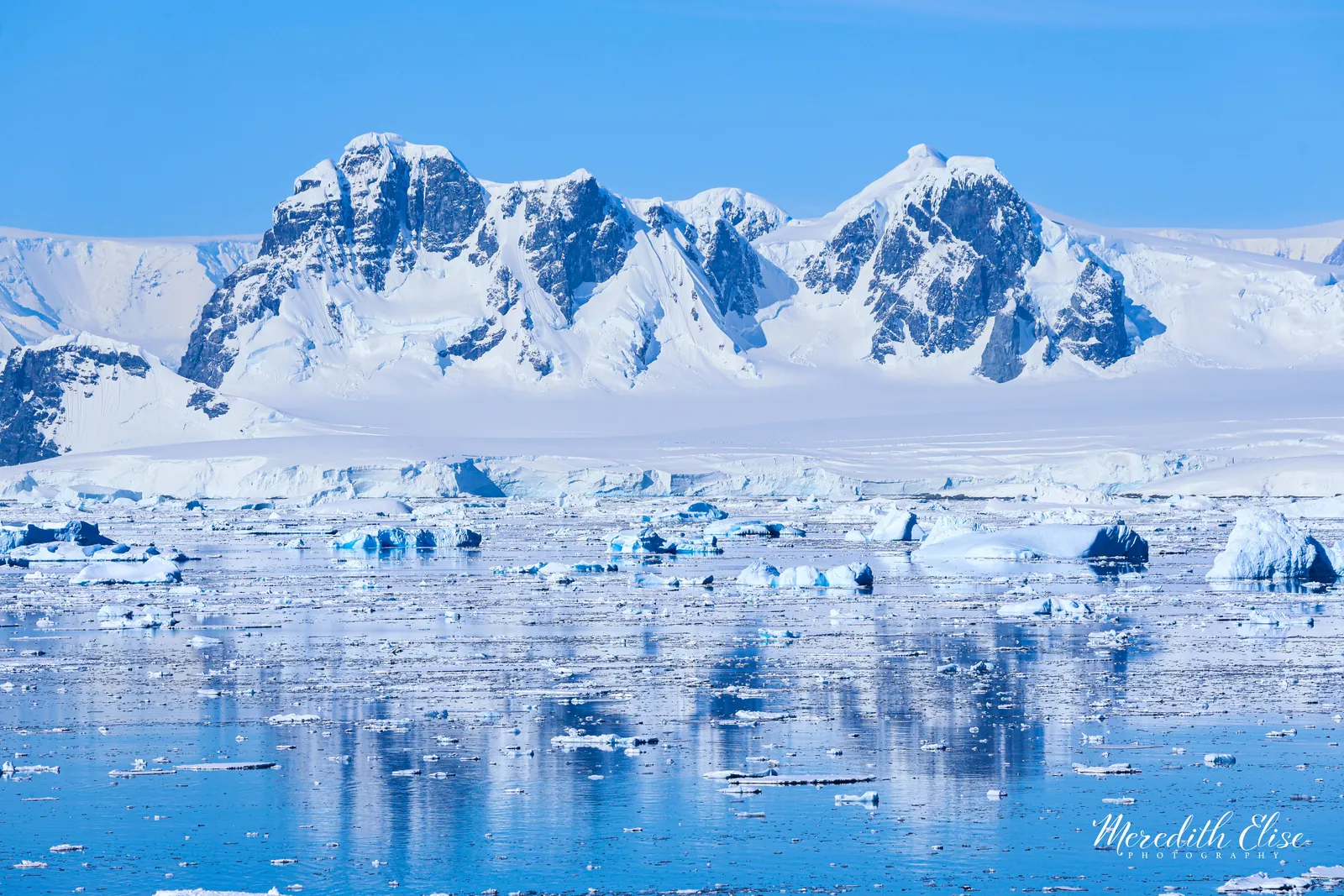 Jagged peaks of the Arrowsmith Peninsula reflected in ice-flecked turquoise water — Antarctica fine art print
