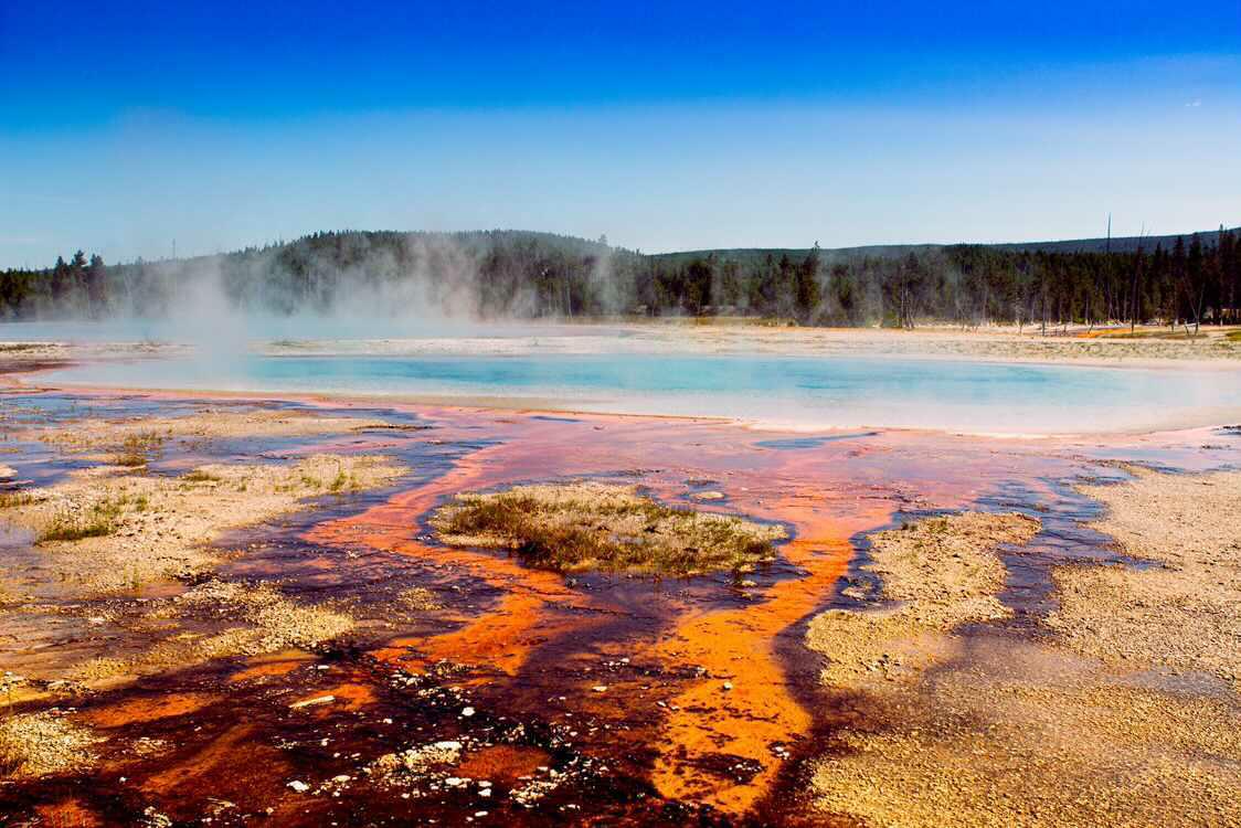 Vivid orange and red bacterial mats surrounding a steaming turquoise hot spring