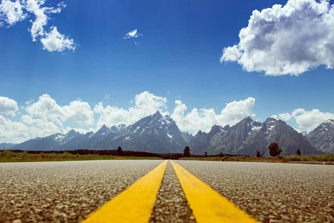 Yellow center lines of a highway leading straight toward the Grand Tetons