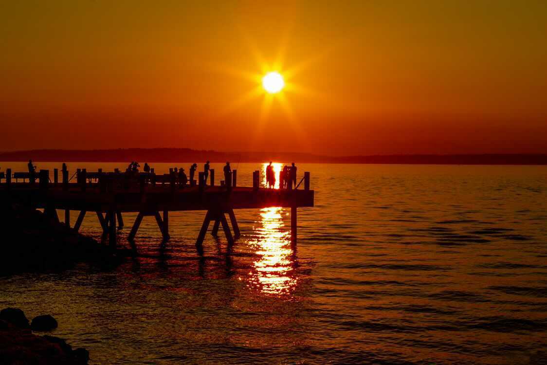 Silhouettes of people on a pier against a blazing orange sunset over calm water