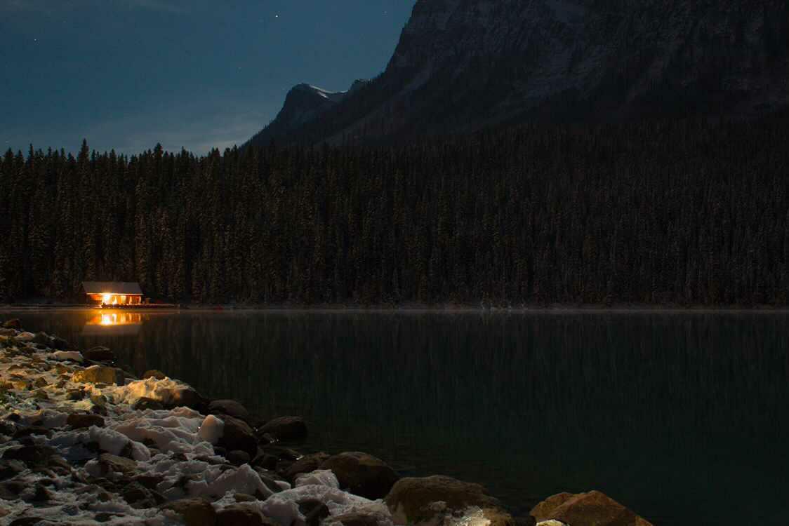 A single glowing cabin reflected in the still midnight surface of Lake Louise