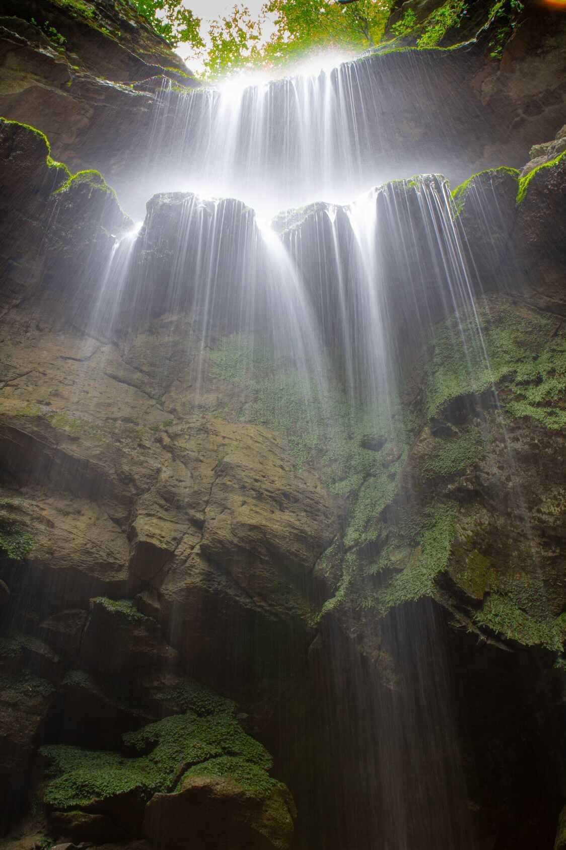 Curtains of water streaming through a mossy cave opening
