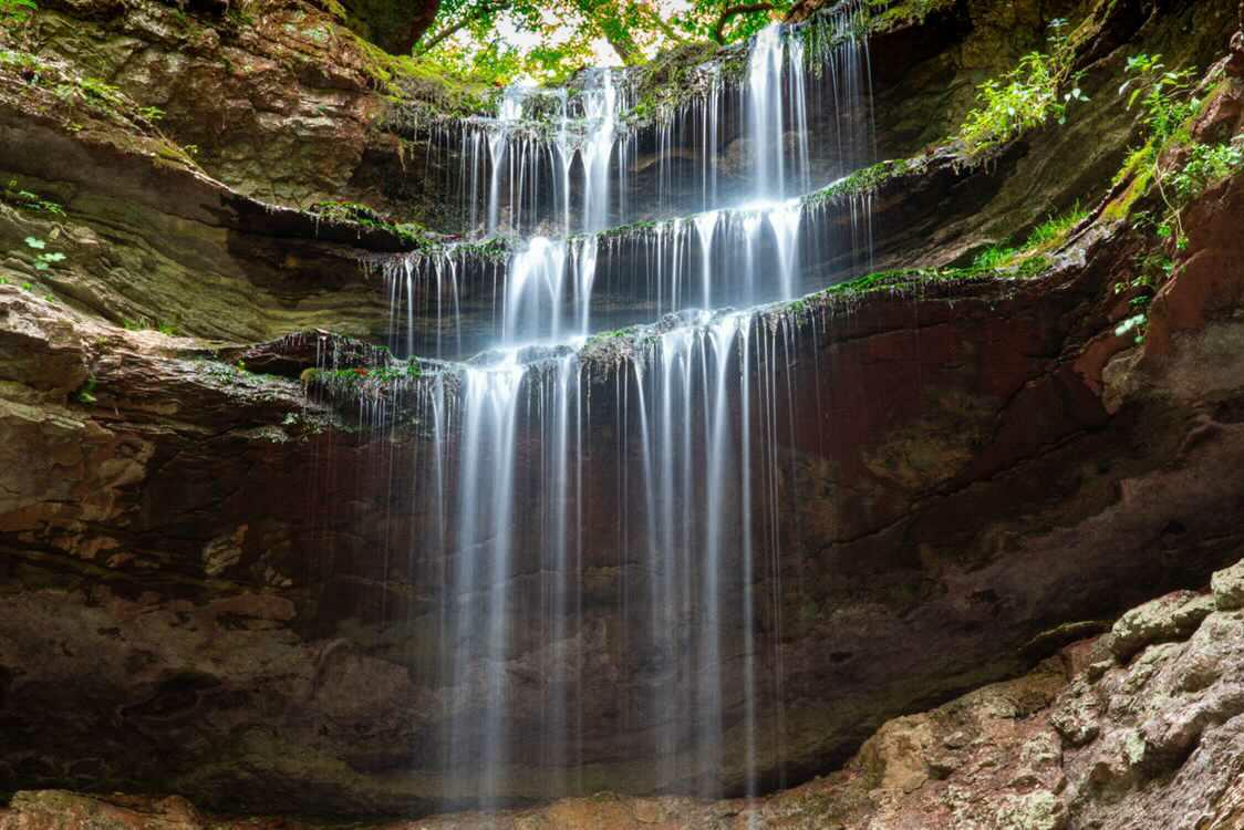 Tiered waterfall cascading over layered rock in an arched grotto