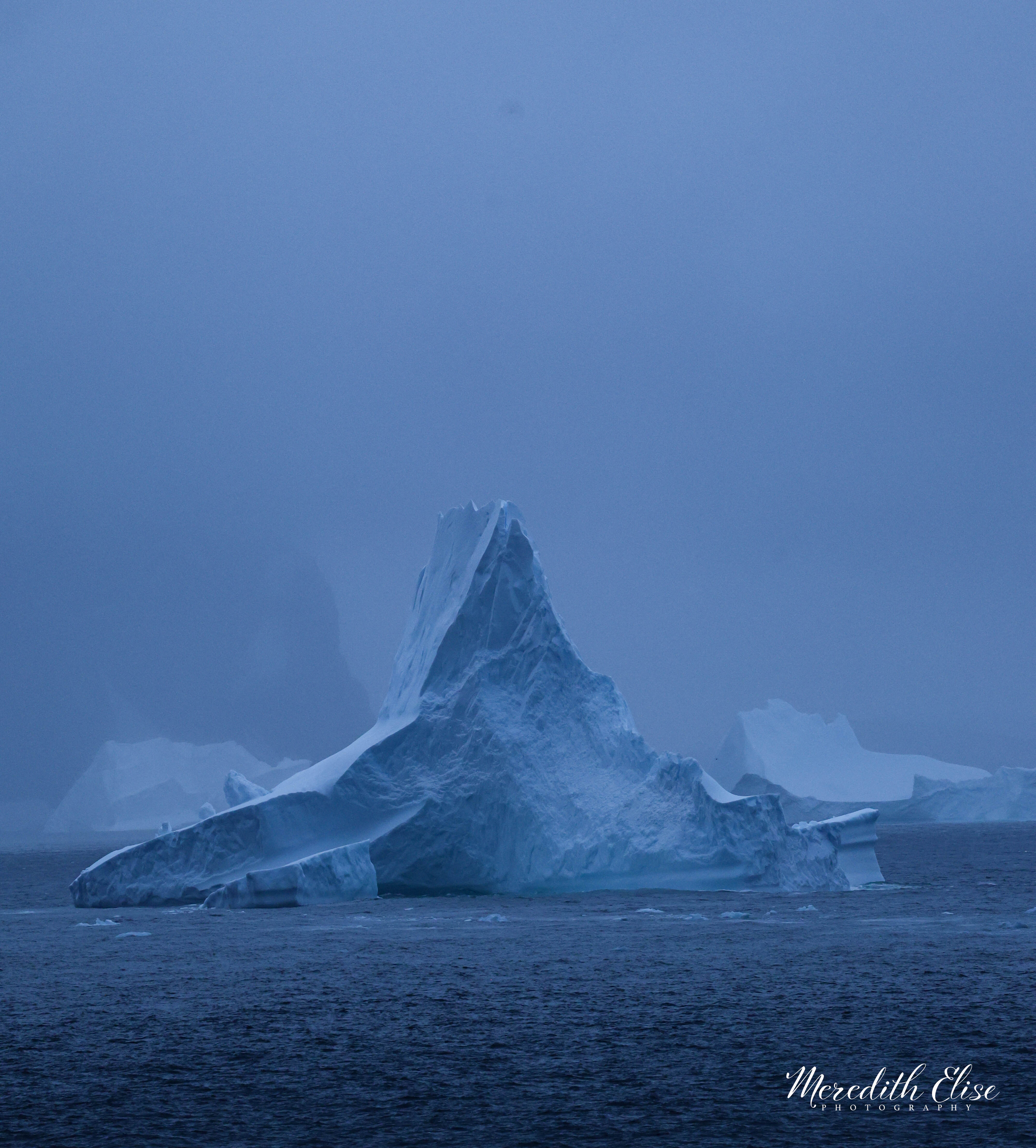 A tall cathedral iceberg rising through blue-grey Antarctic mist