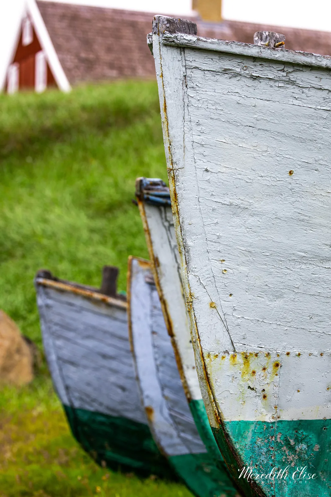 Bows of weathered wooden fishing boats resting in the grass of a Greenland village — fine art print